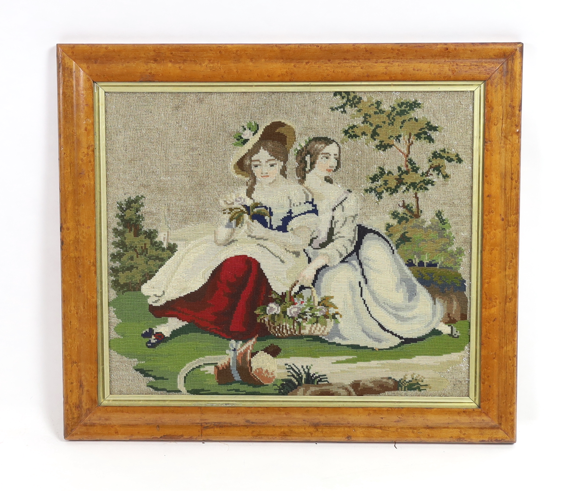 A 19th century maple framed Berlin beadwork embroidery of two young girls, possibly Queen Victoria’s daughters, seated with a basket of flowers in a garden, the sky embroidered with white beads, 49cm wide x 42cm high